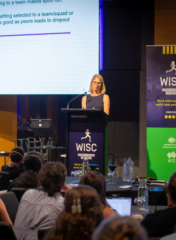 Michelle Smith is standing up at the podium at the Women In Sport Congress. 